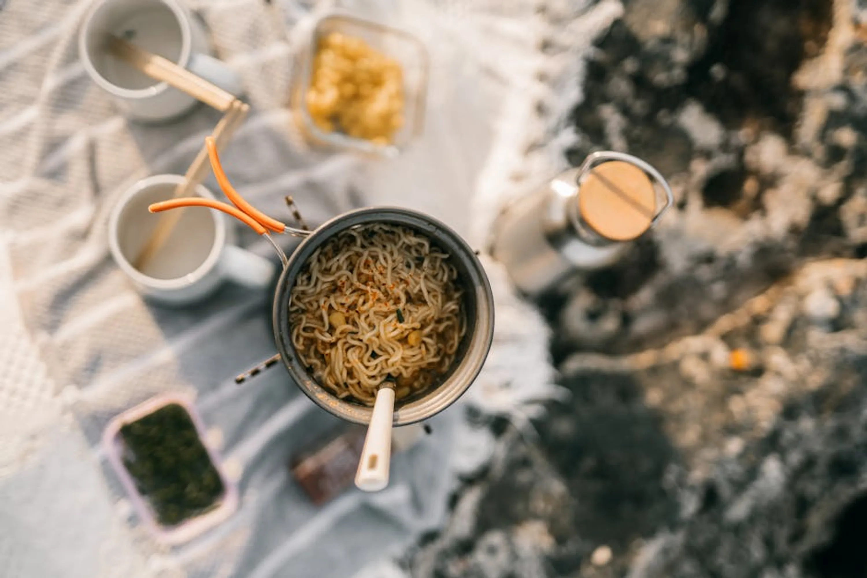 Top view of instant noodles cooking during a camping trip, with various outdoor kitchen essentials. Instant Pot cooking a hearty stew