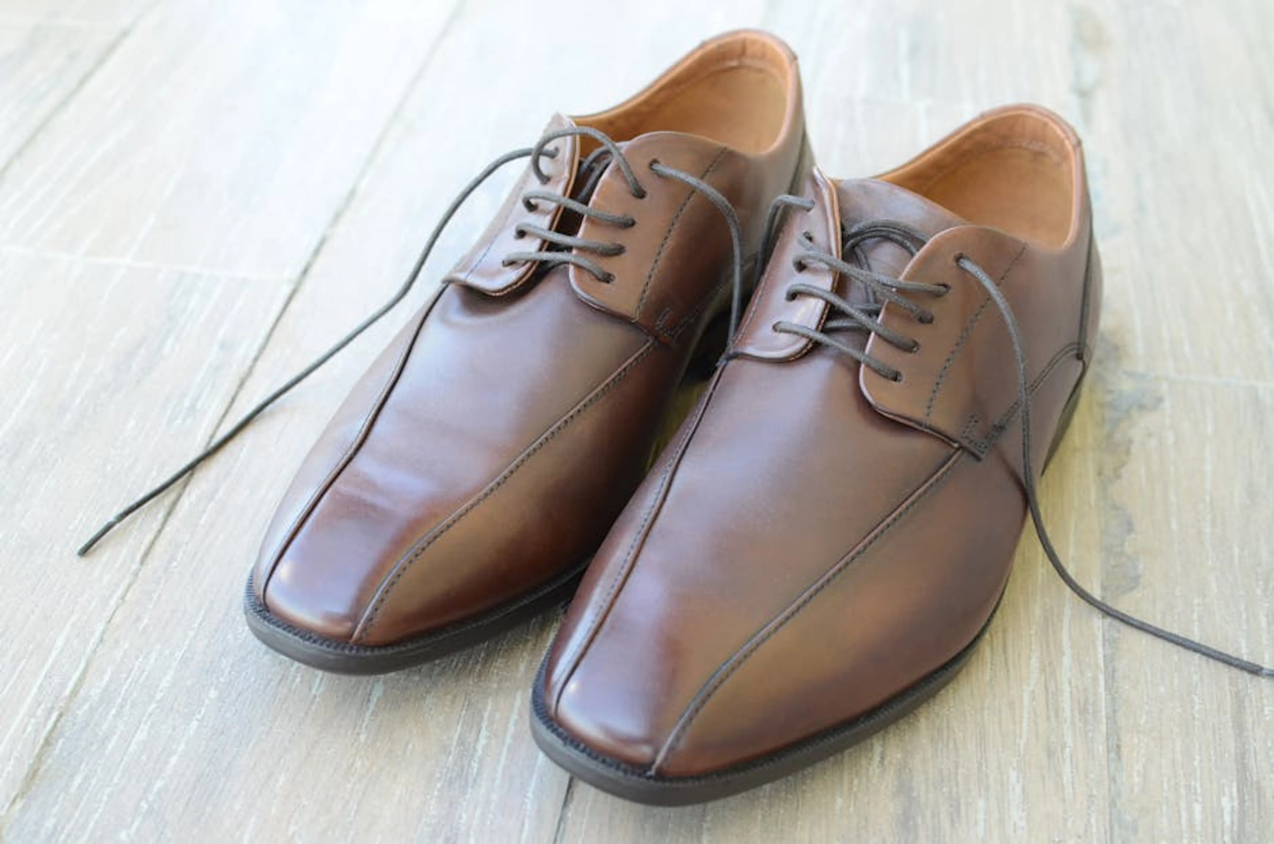 A pair of elegant brown leather dress shoes with shoelaces on a wooden floor, showcasing luxury and style. A selection of neutral-colored, mix-and-match clothing items laid out for packing.