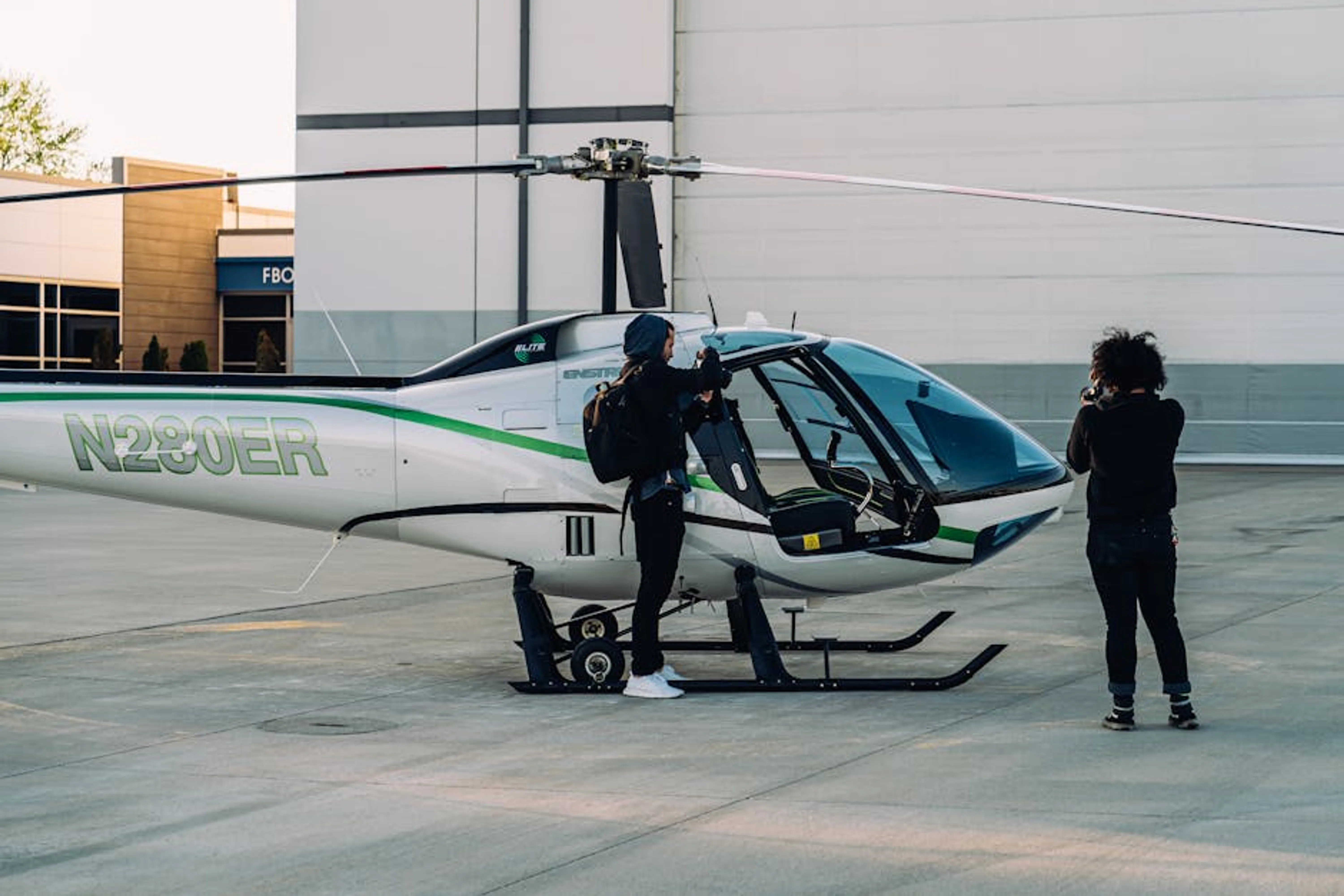 Two photographers capturing a helicopter on a sunny day outdoors. Various essential packing gear items laid out, including packing cubes, travel bottles, and a universal adapter.