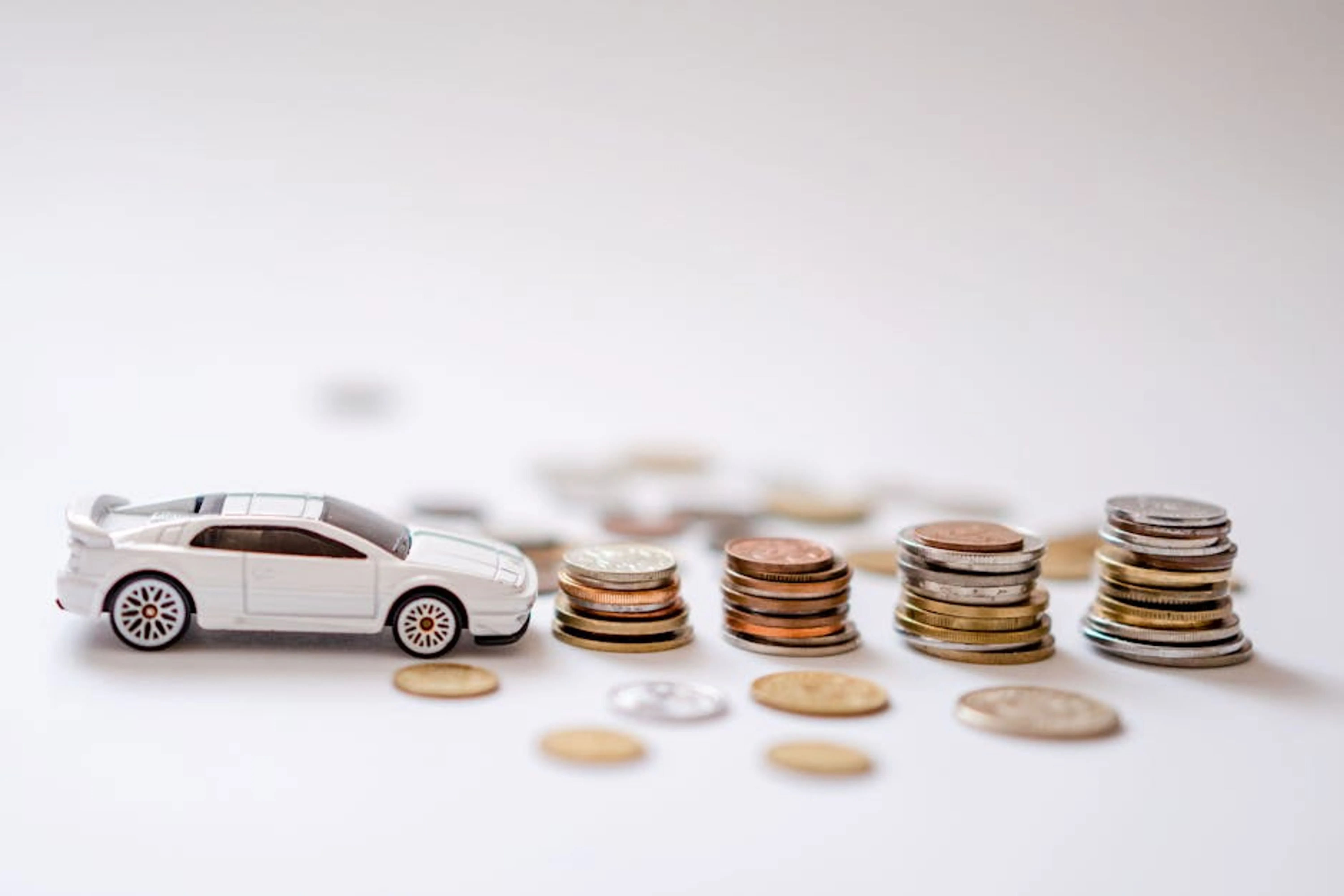 White toy sports car beside stacks of coins on a white background, emphasizing savings and finance. Person calculating car ownership costs on a calculator