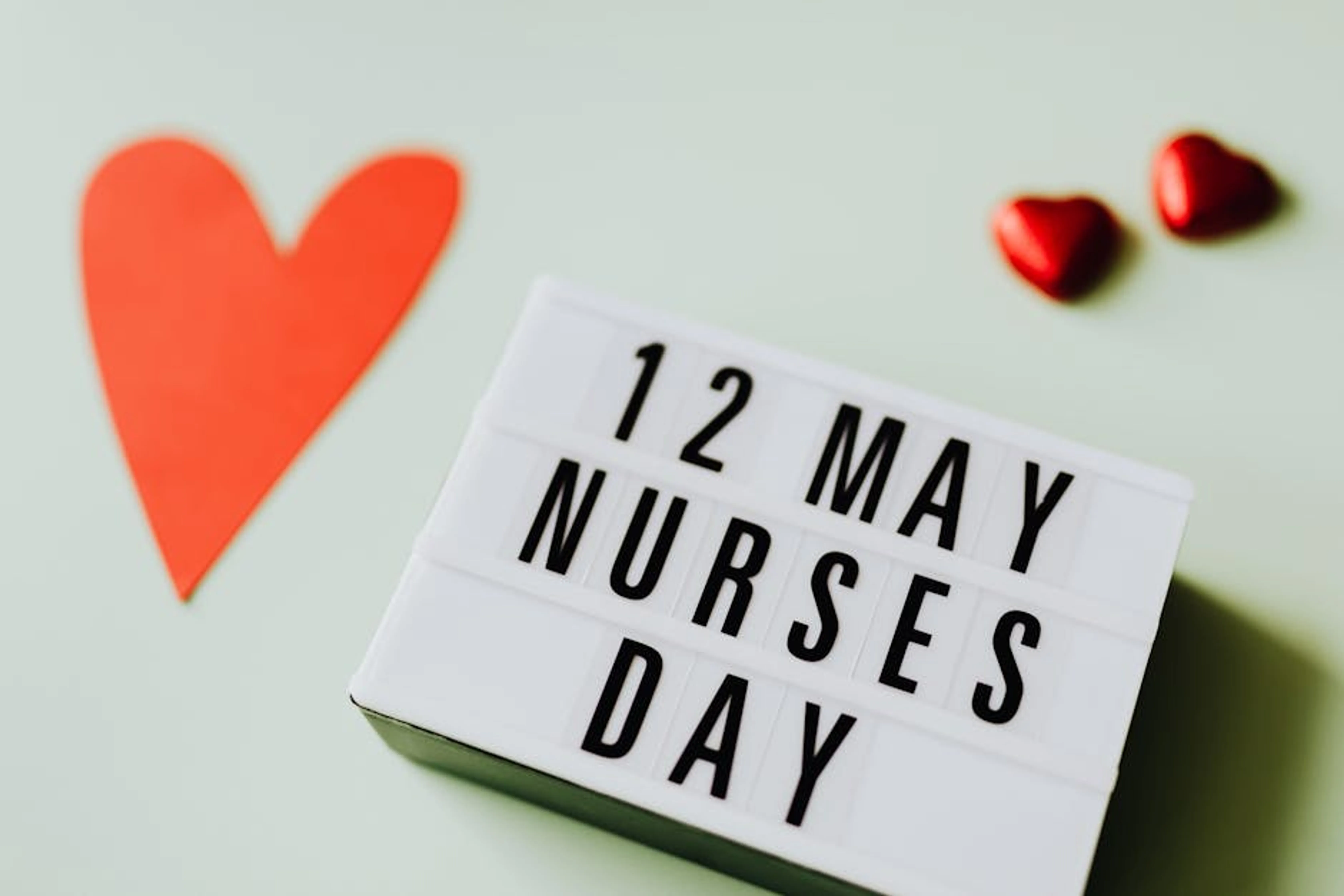 Festive display celebrating Nurses Day on May 12 with heart symbols. An image depicting a nurse interacting with a patient in a hospital setting, symbolizing the core of the nursing profession.