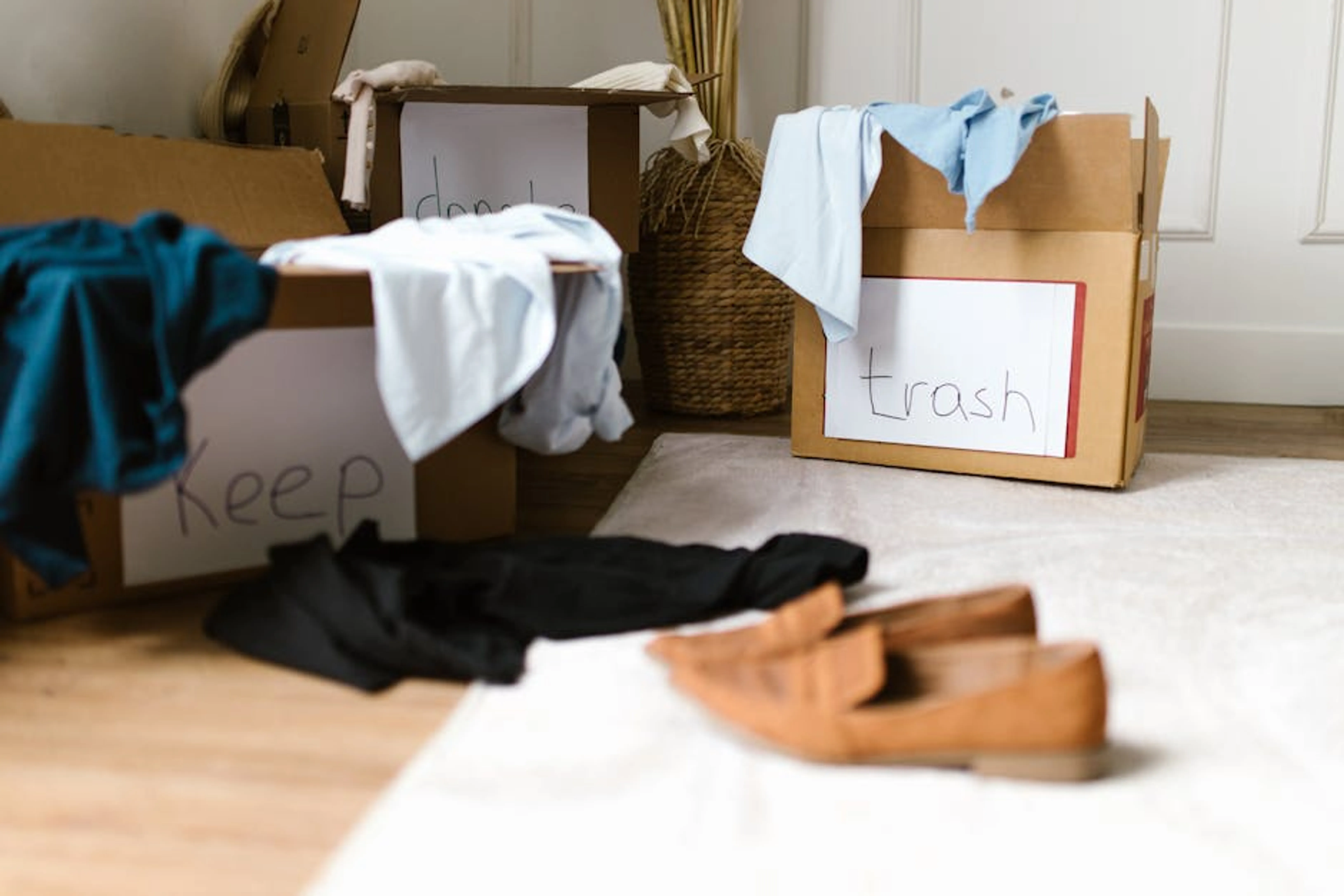 Decluttering concept using labeled boxes for sorting clothes in a home setting. Person sorting through items in a living room, deciding what to keep or discard, illustrating the decluttering process.