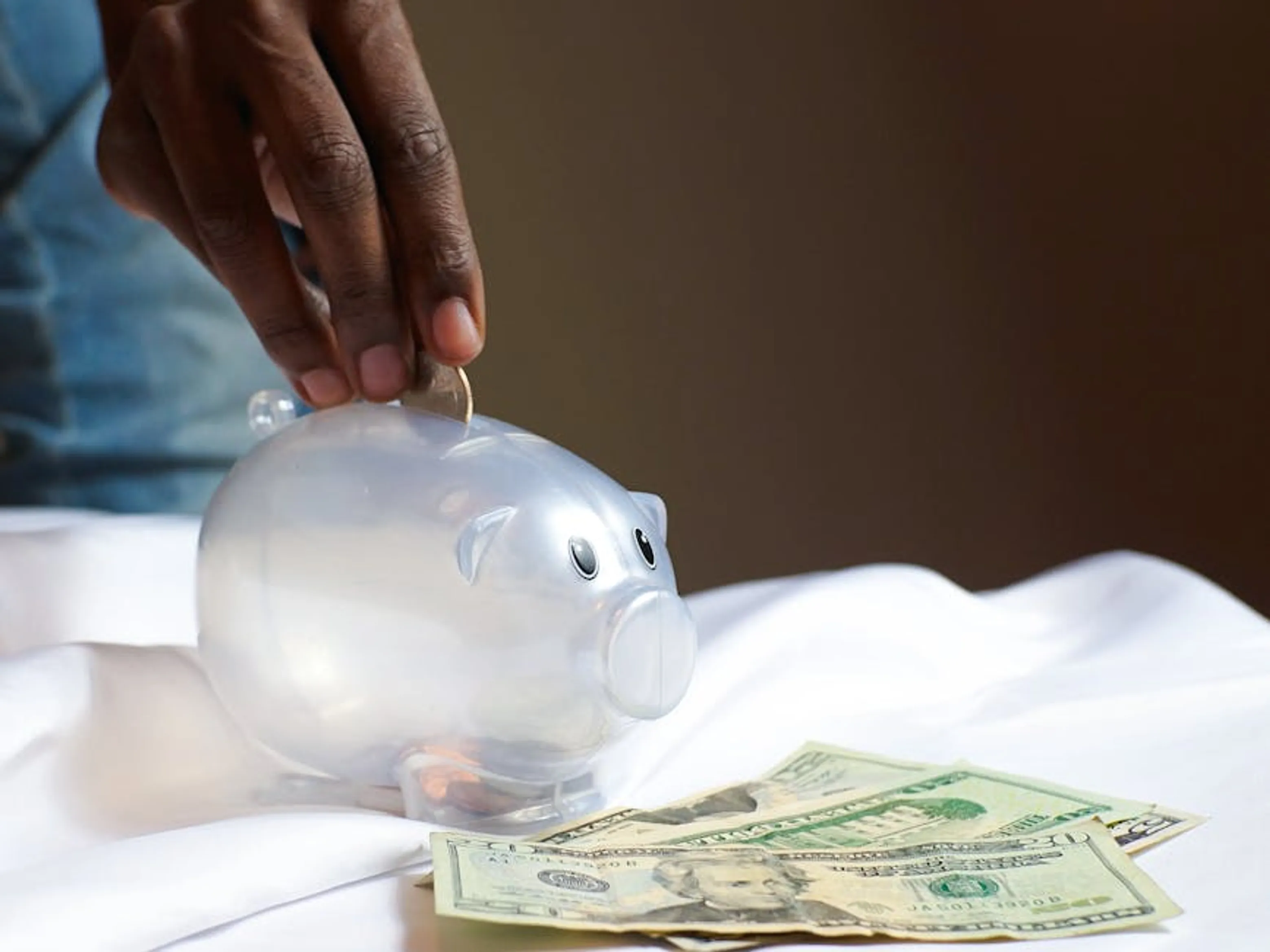 A hand placing a coin in a piggy bank with dollar bills nearby signifying savings and finance. A person diligently organizing financial documents and bills, symbolizing consistent financial discipline
