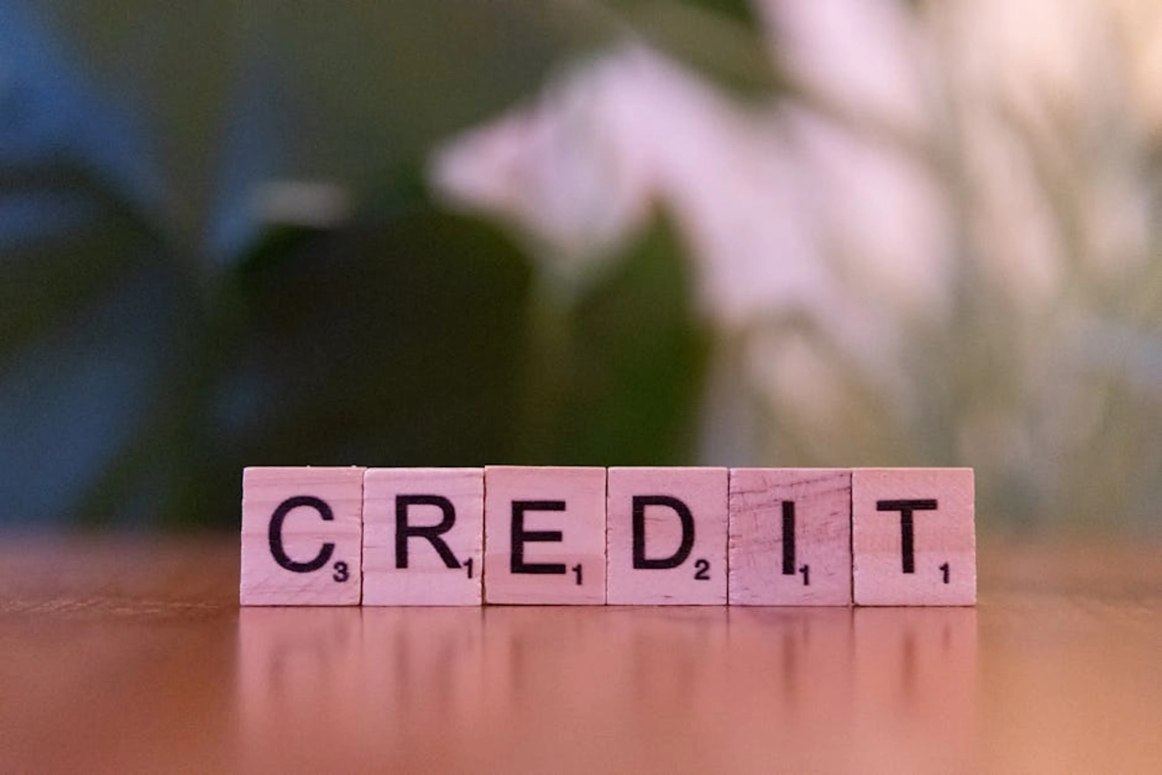 Close-up of wooden blocks spelling 'credit' with a blurred leafy background. A visual representation of a credit score chart showing different score ranges and their implications.