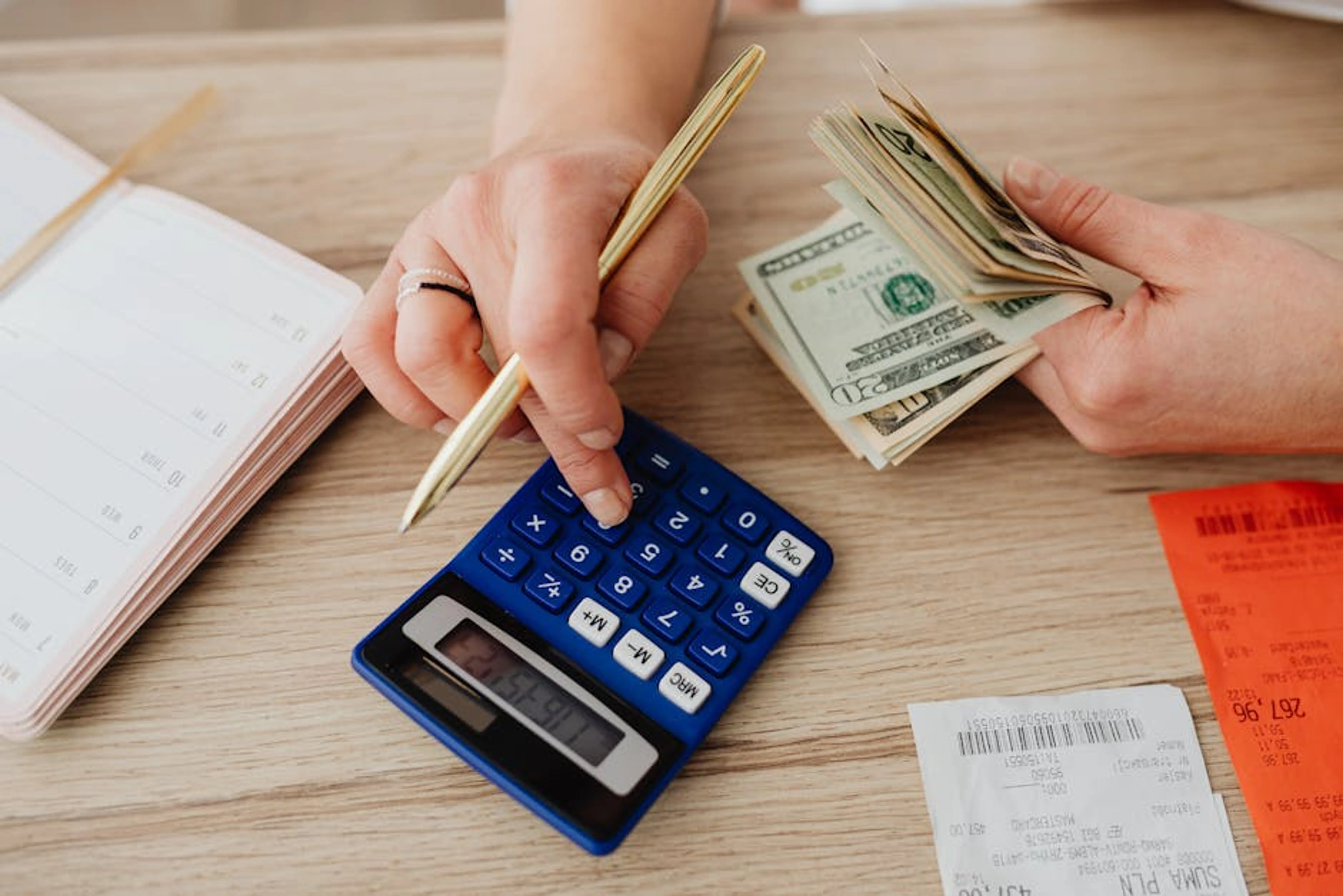 Hands handling cash and calculator for budget planning. Modern financial scene. Family looking at a calendar, planning for upcoming irregular expenses like school fees or car maintenance