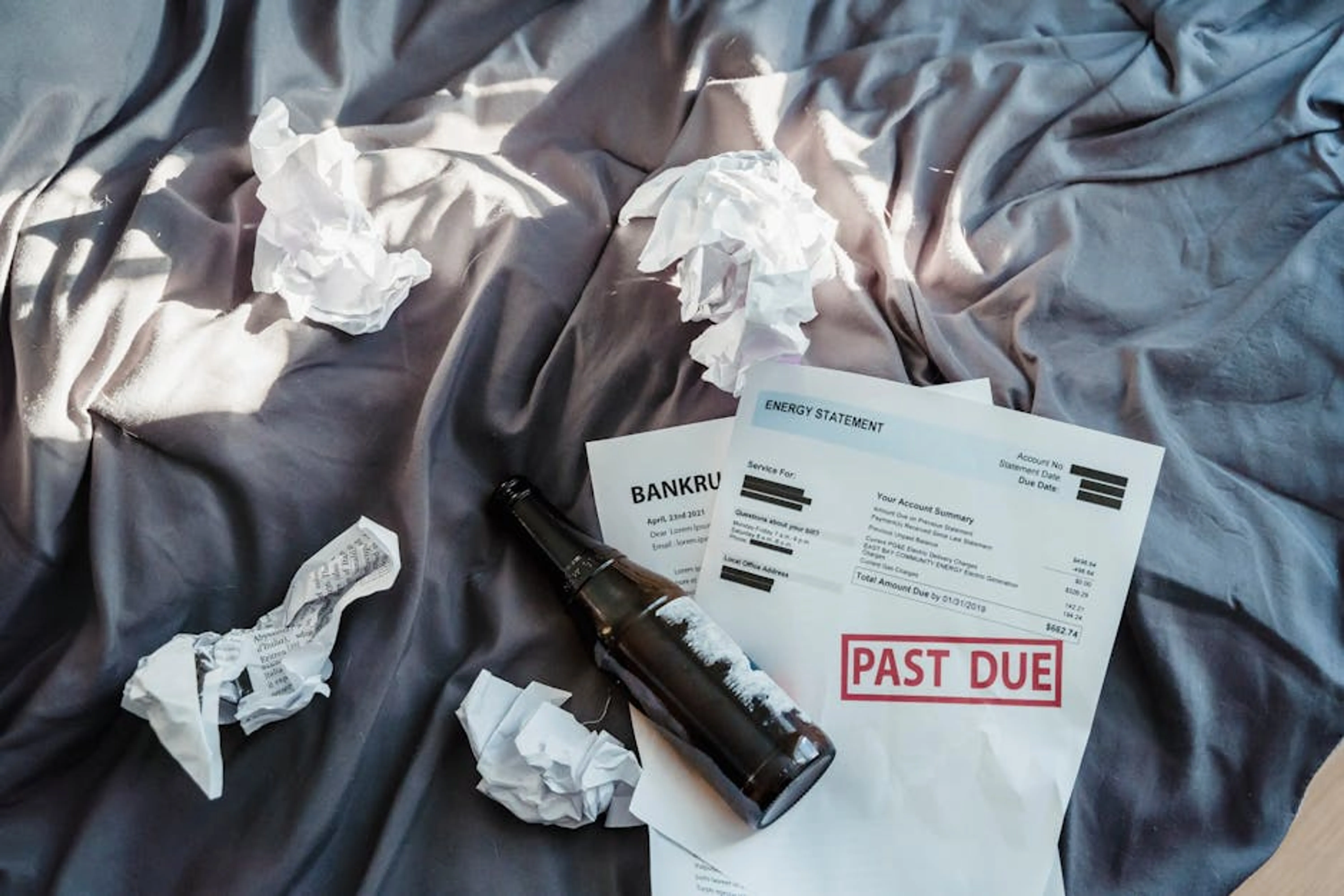 Scene of financial distress with bankruptcy notice, past due bills, and crumpled papers on a bed. Calendar showing overdue payment reminders