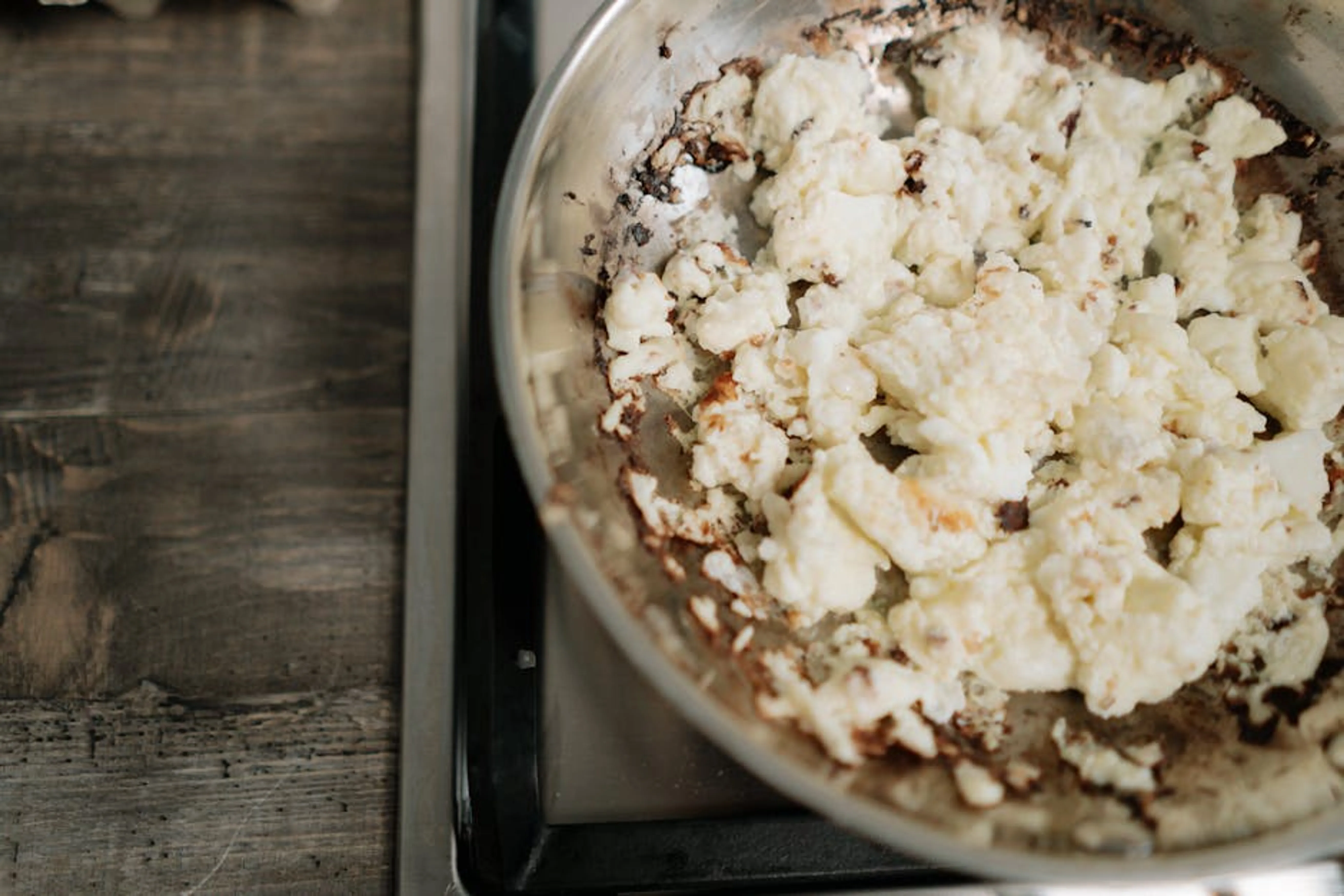 Overcooked scrambled eggs in a stainless steel skillet on a stove. A close-up image of a burnt pan with scorched food residue at the bottom, illustrating the common problem of burning food.