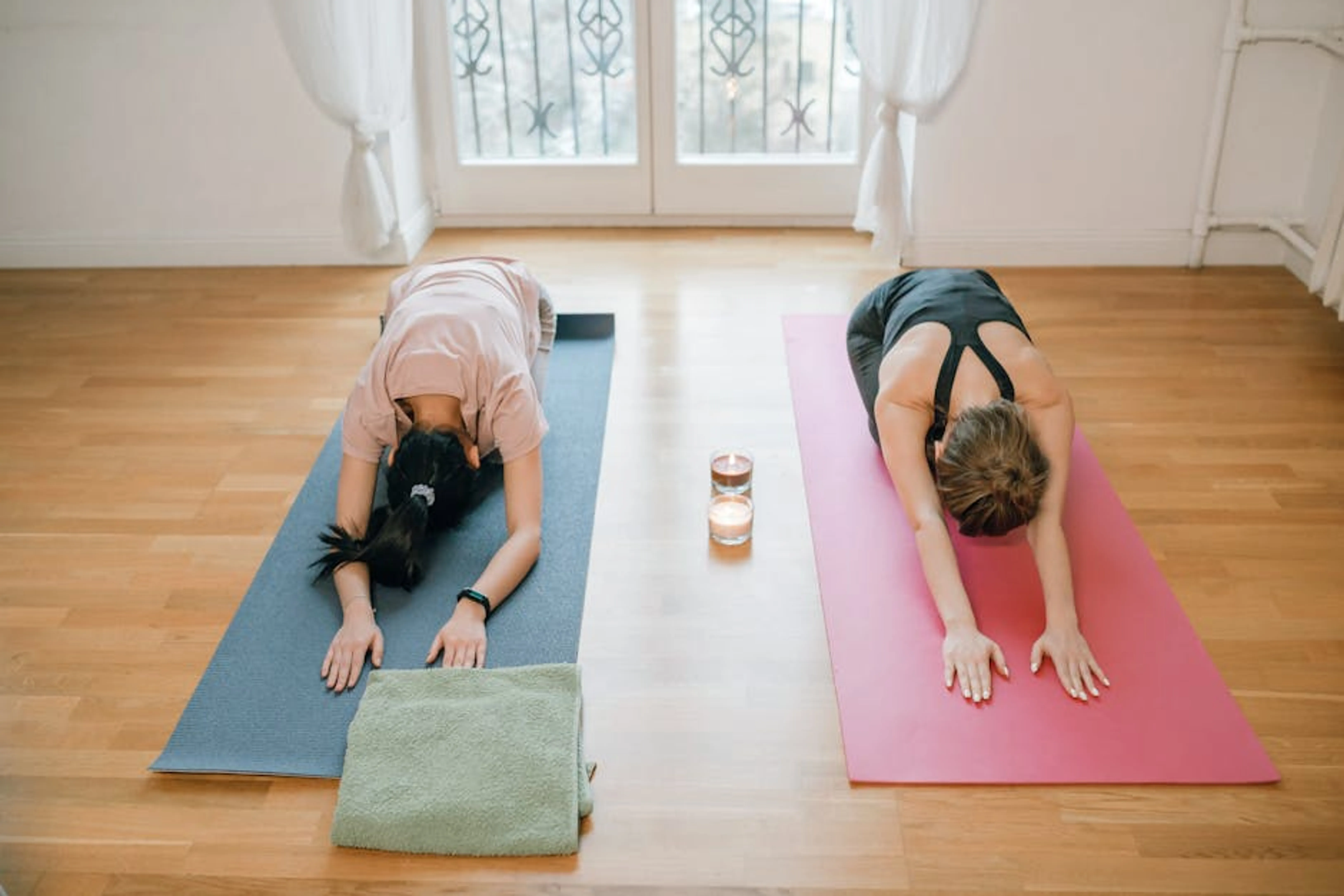 Two women performing yoga poses on mats indoors, promoting relaxation and mindfulness. Person happily exercising in a comfortable home environment