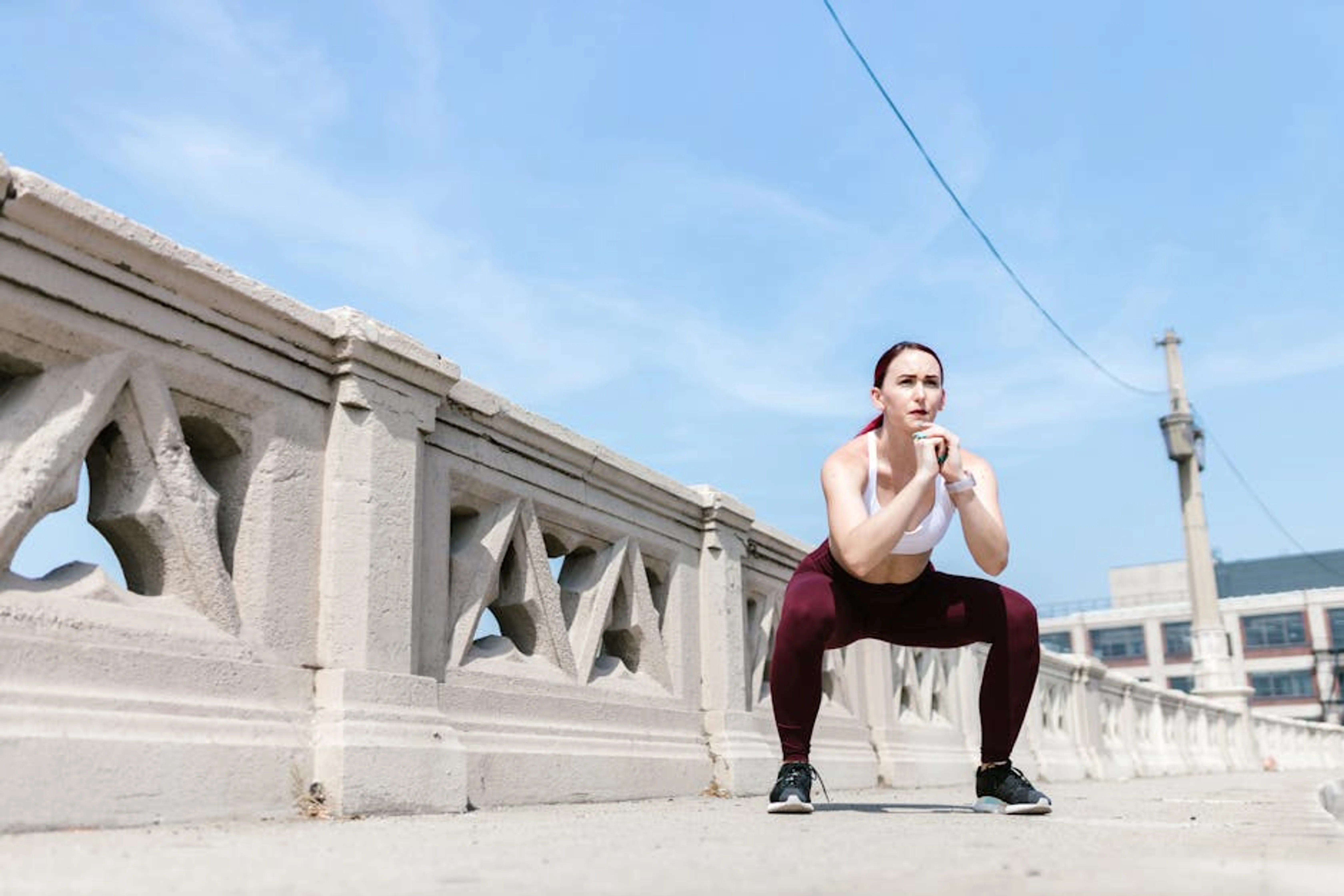 Woman performing a squat exercise outdoors beside a concrete railing under a clear sky. A person performing a perfect bodyweight squat in a home setting