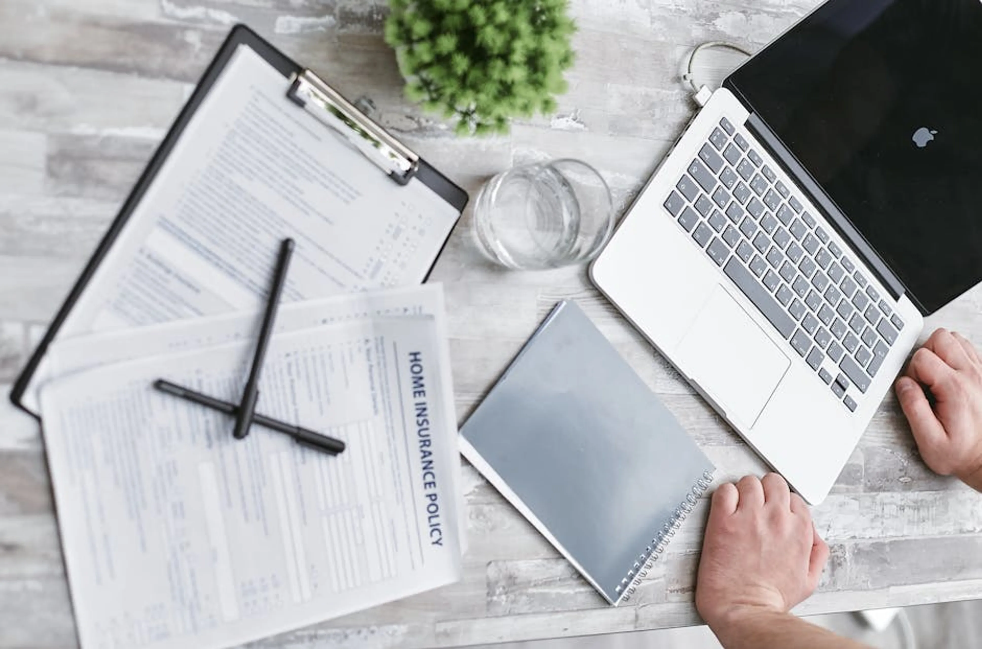 Top view of home insurance forms, laptop, and documents on a desk, conveying a professional office setting. An open suitcase on the floor of a modern apartment, surrounded by personal belongings, symbolizing renters insurance protection.