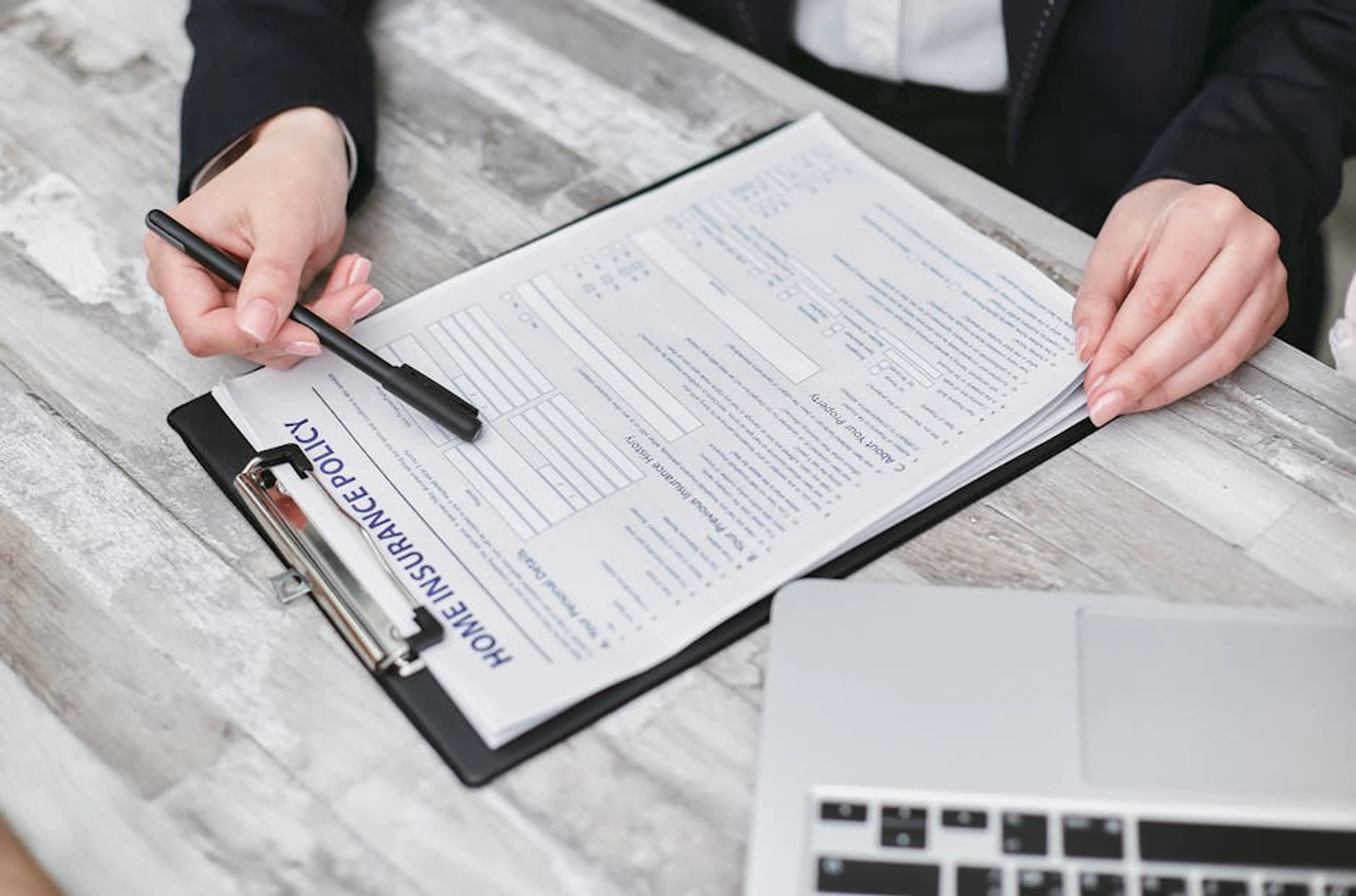 Close-up of hands reviewing a home insurance policy, emphasizing professionalism and finance. A person's hand holding a magnifying glass over an insurance document, with a piggy bank and calculator nearby, symbolizing policy review for savings.