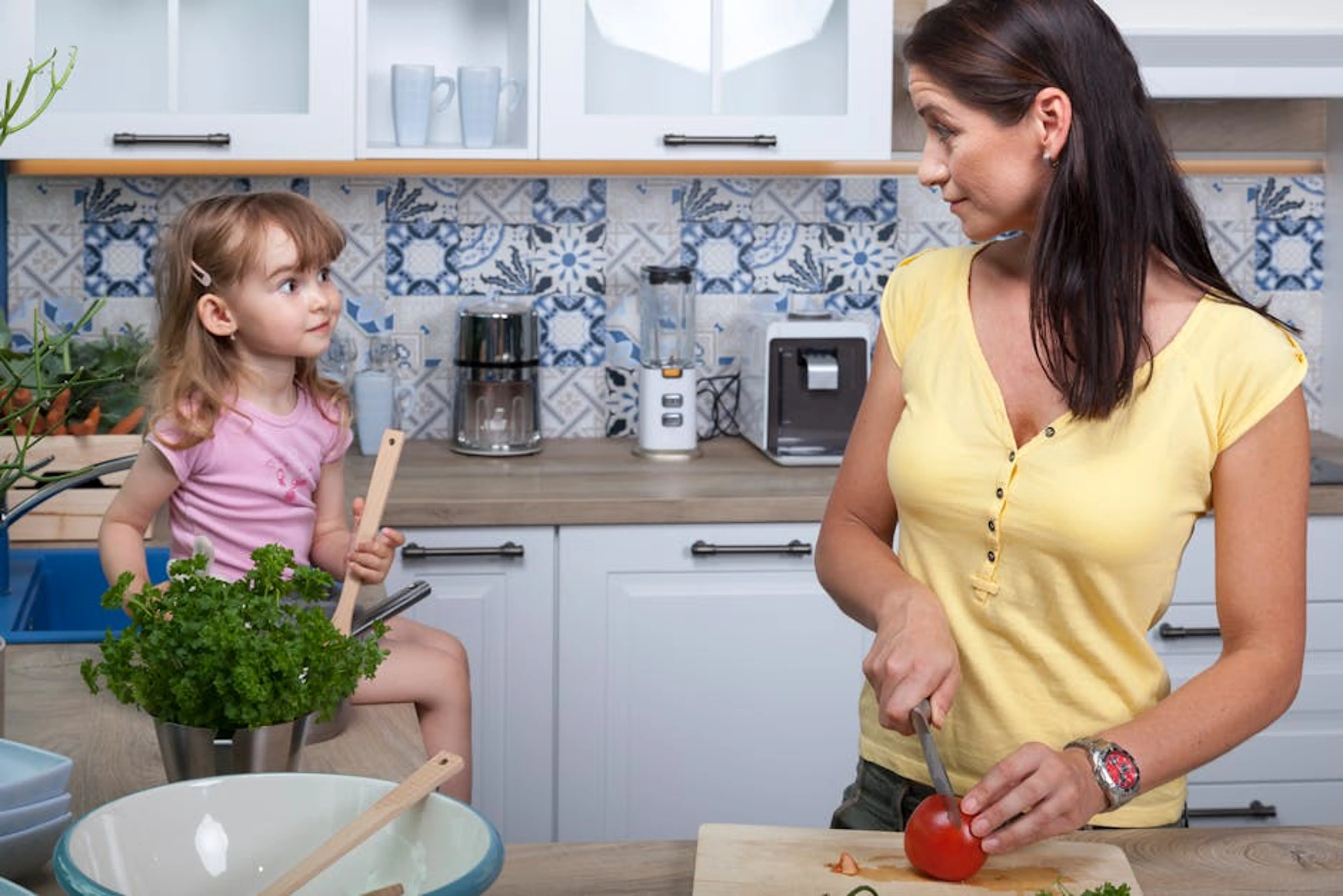 A mother and daughter enjoy cooking together in a cozy modern kitchen, fostering family bonds. Parent and child engaged in active listening and empathetic conversation