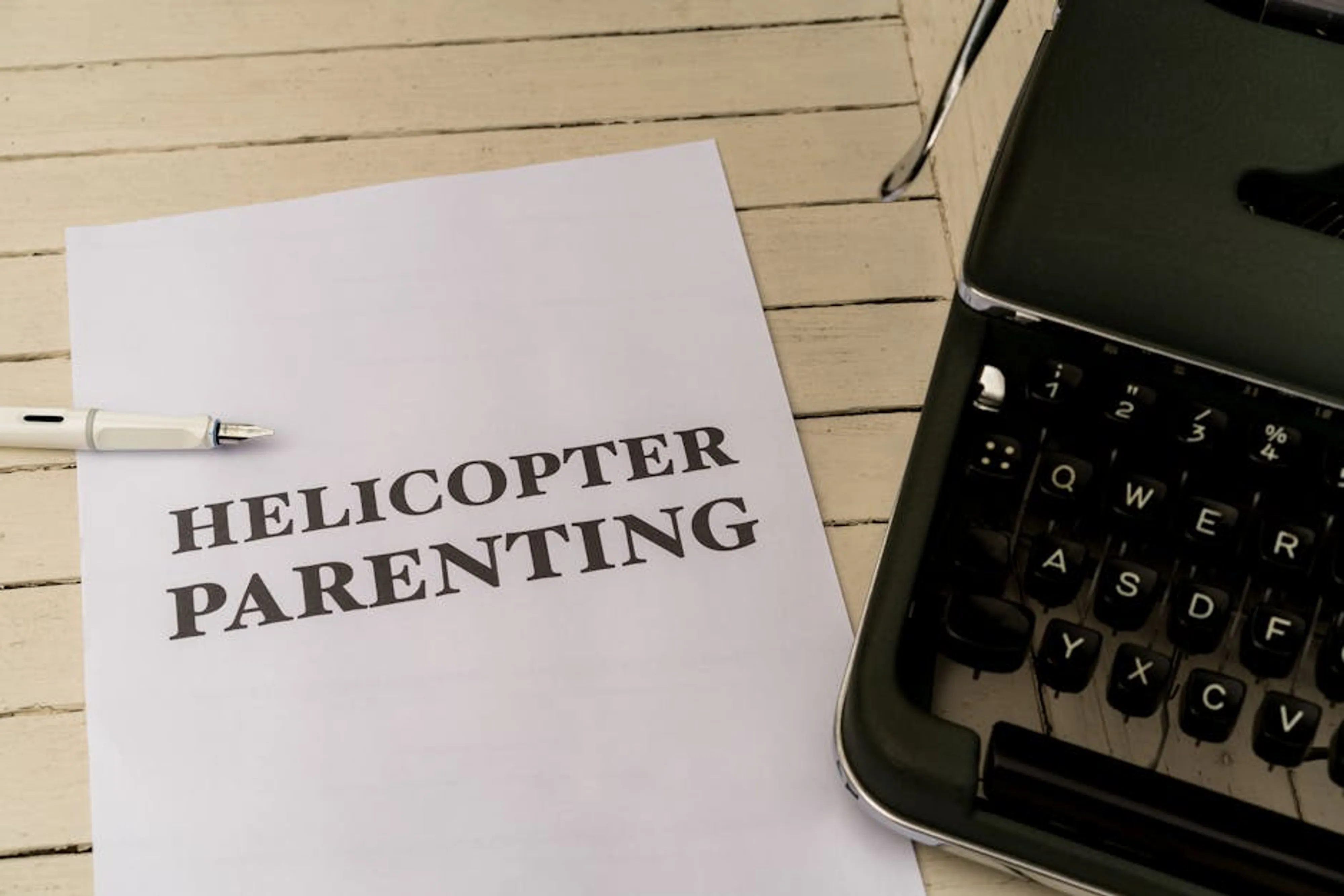 Paper with 'Helicopter Parenting' text next to a typewriter and pen Parent and child walking together, showing balanced support and independence