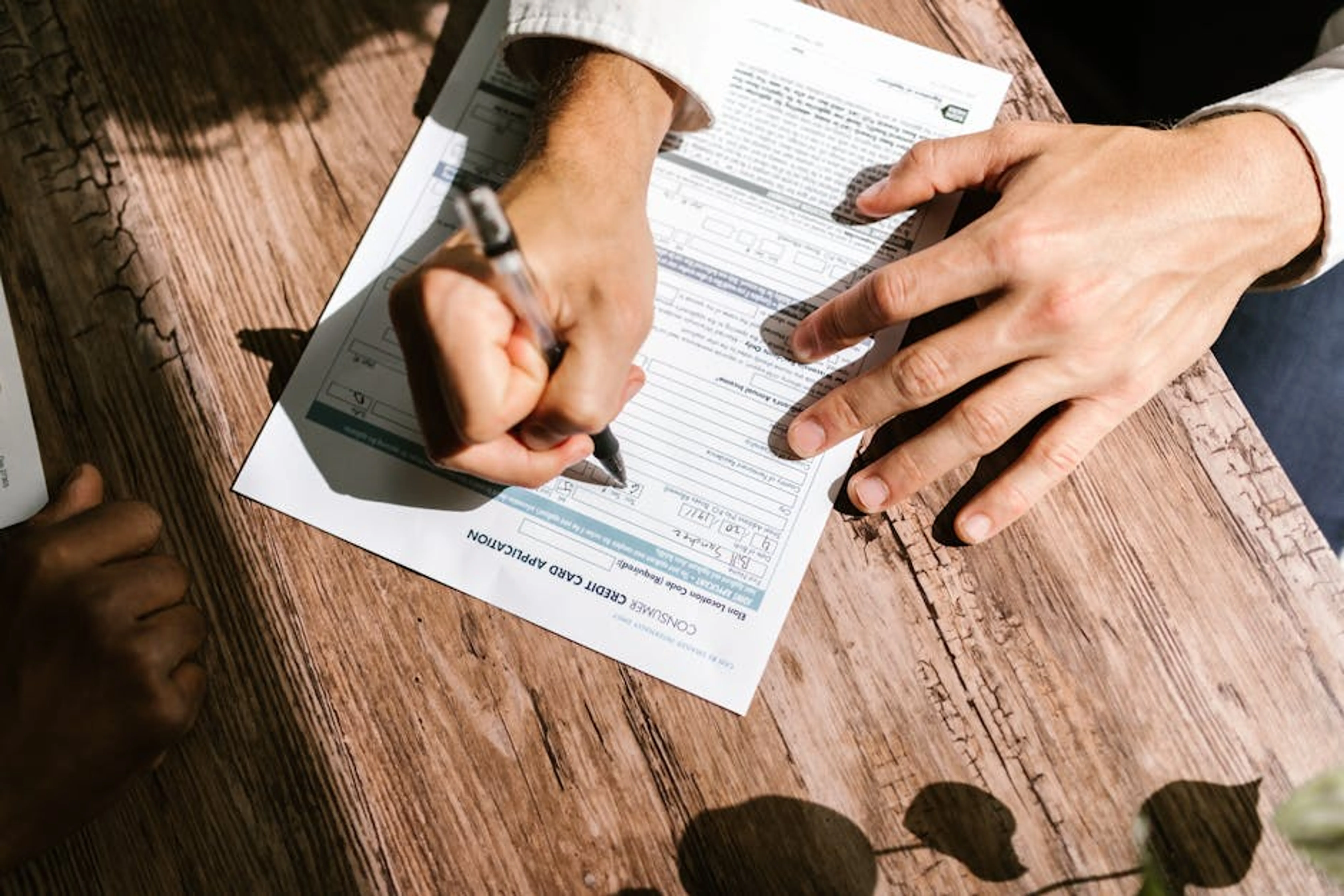 Hands writing on a consumer loan credit application form on a wooden table. Close-up of a hand filling out a loan application form