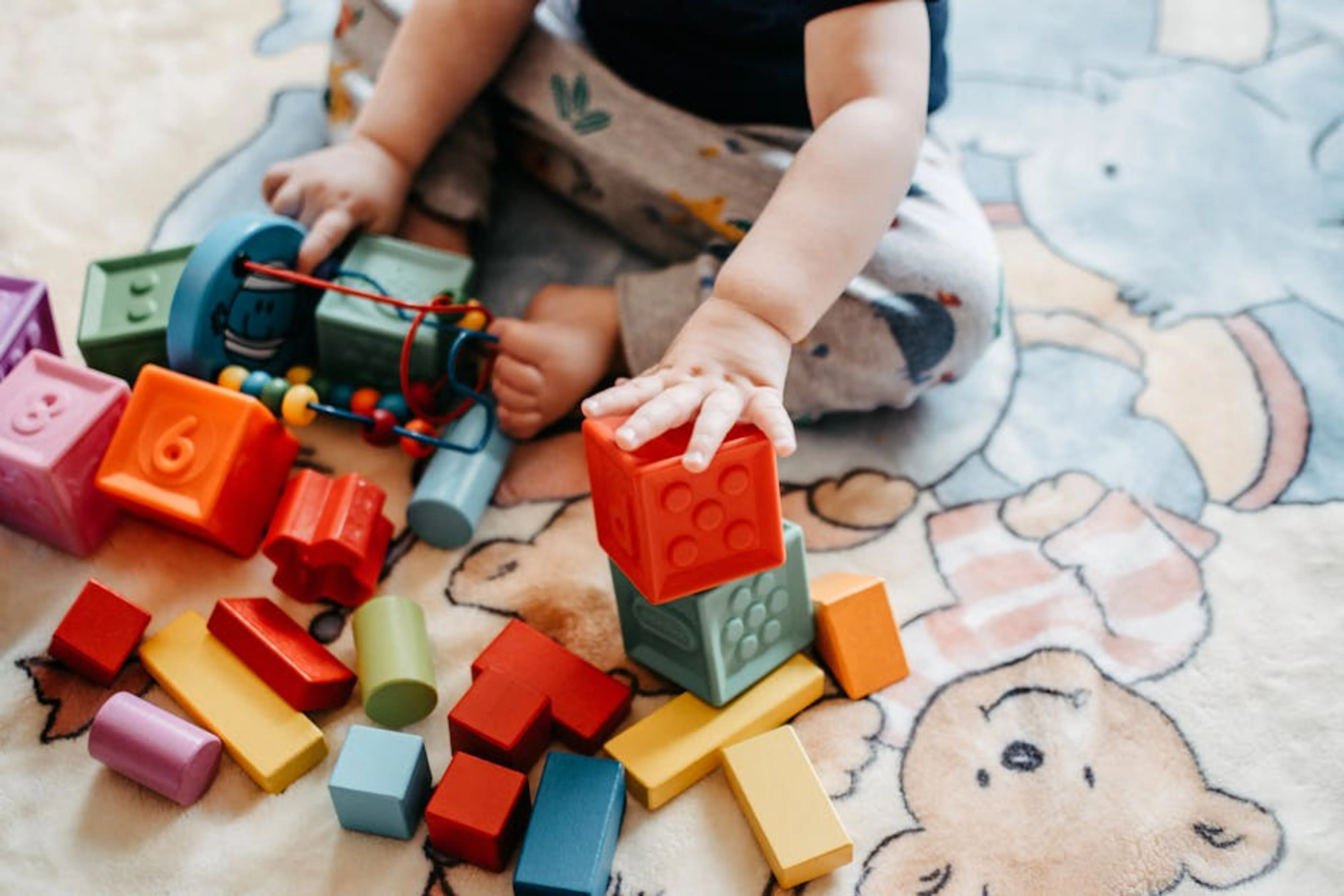 Toddler engaging with vibrant toy blocks on a patterned rug in a playful setting. Toddler stacking colorful building blocks on a playmat