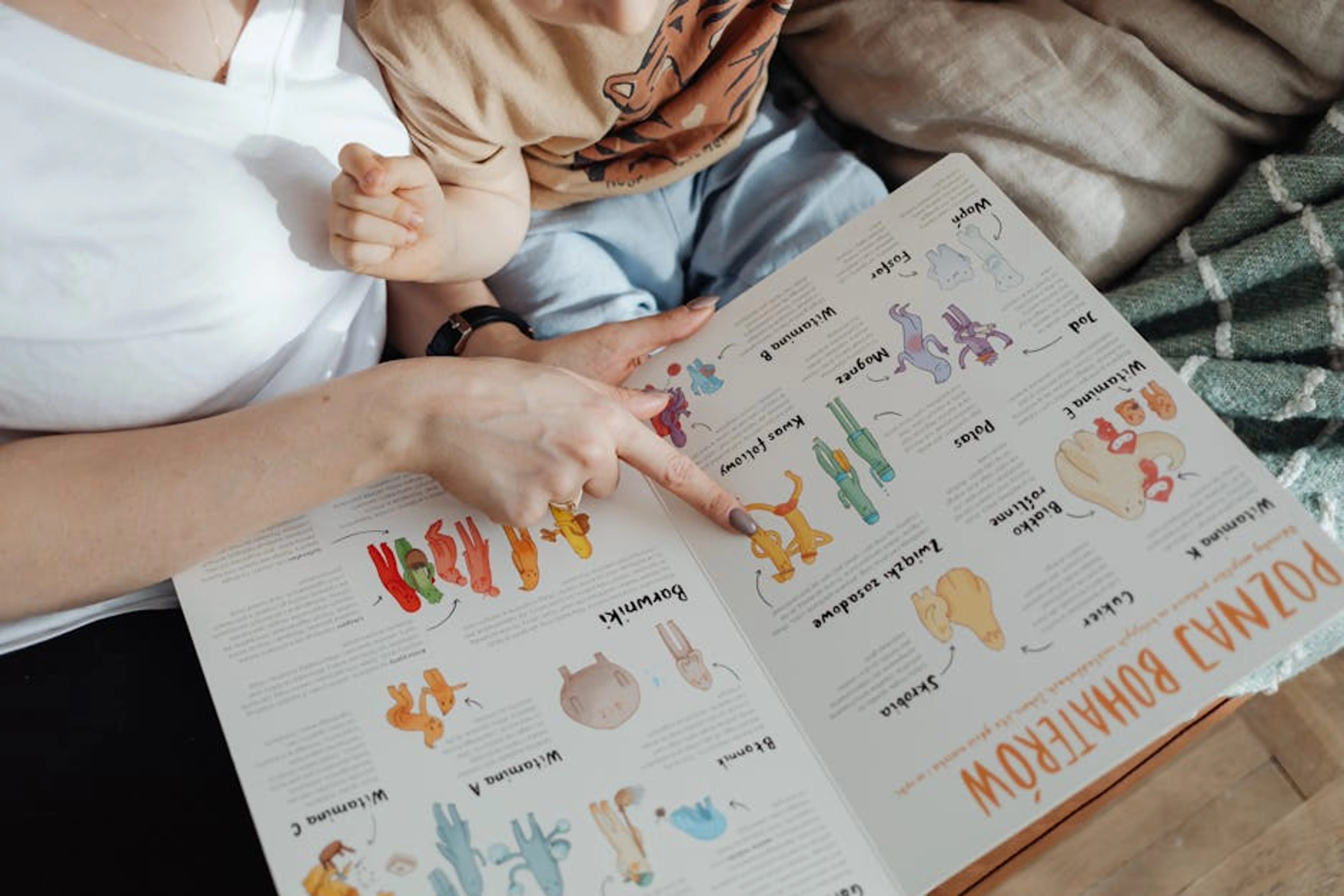 A comforting moment of a mother reading a colorful picture book with her child. Toddler sitting on a colorful rug, looking at a picture book with an adult's hand pointing