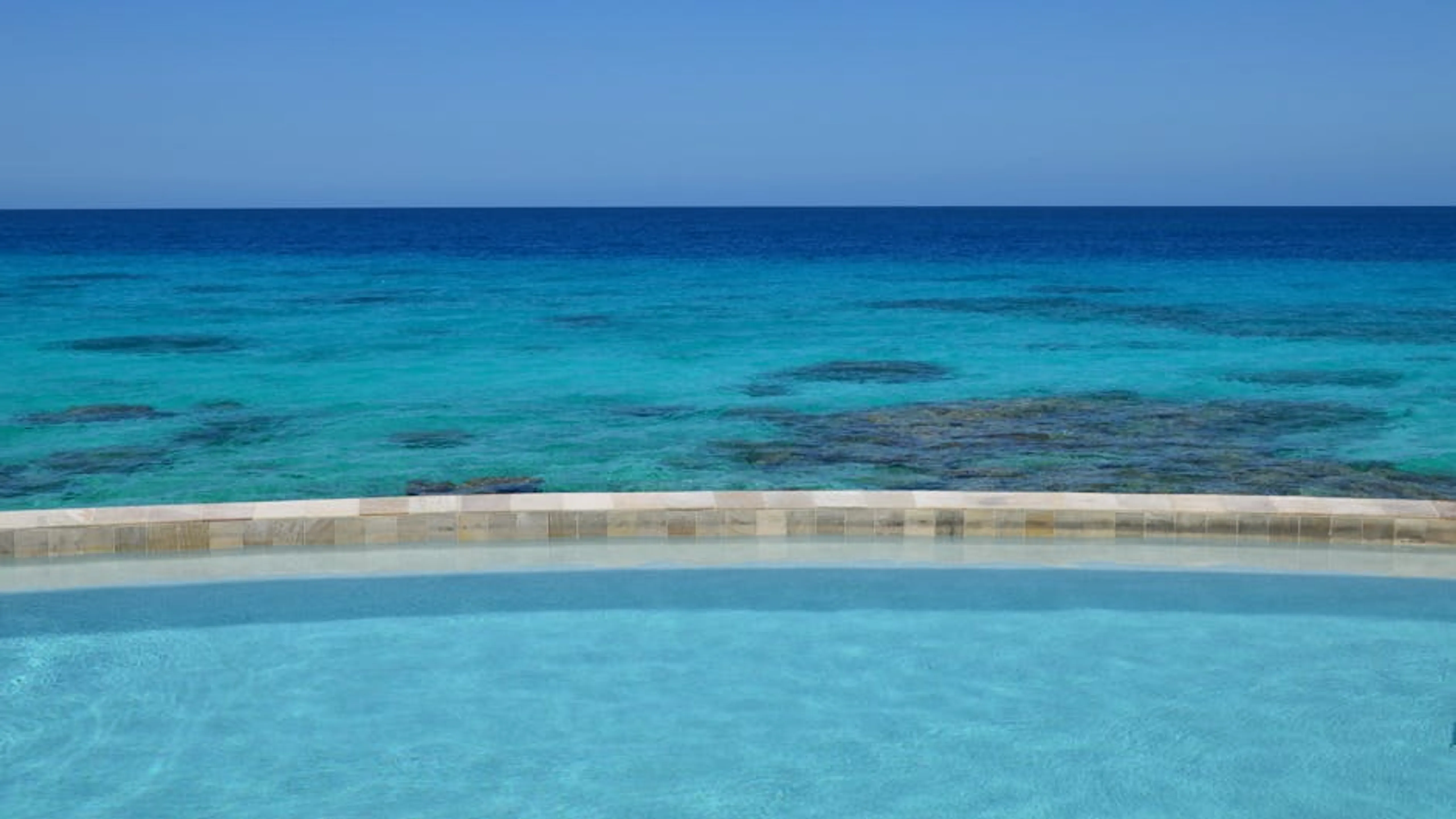 Infinity pool with a breathtaking view of the turquoise ocean on a clear sunny day. Stunning infinity pool overlooking a tropical beach at a luxury resort