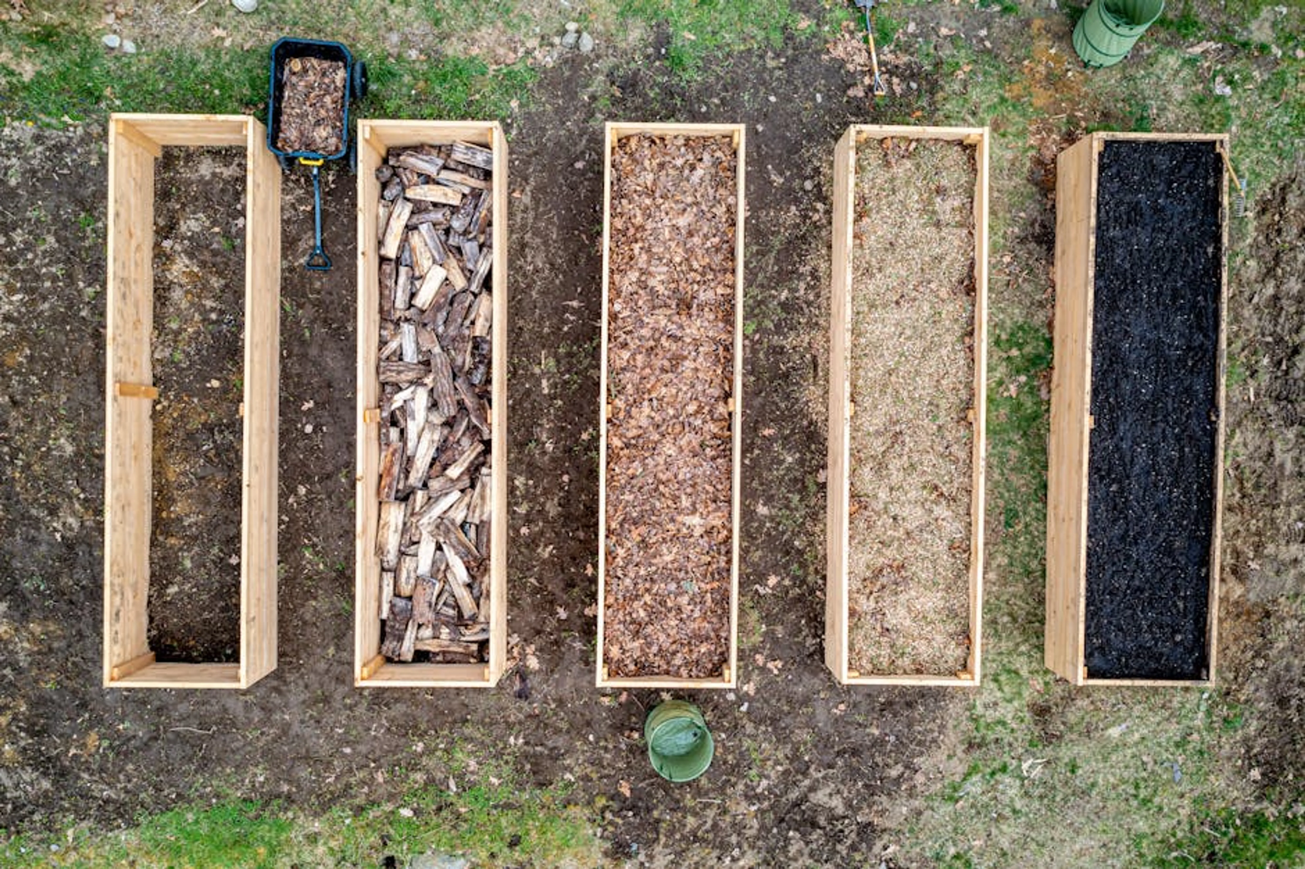 Top view of wooden boxes with piles of firewood wood chips sawdust and coal placed on ground in agricultural plantation A newly constructed raised garden bed being filled with soil and compost