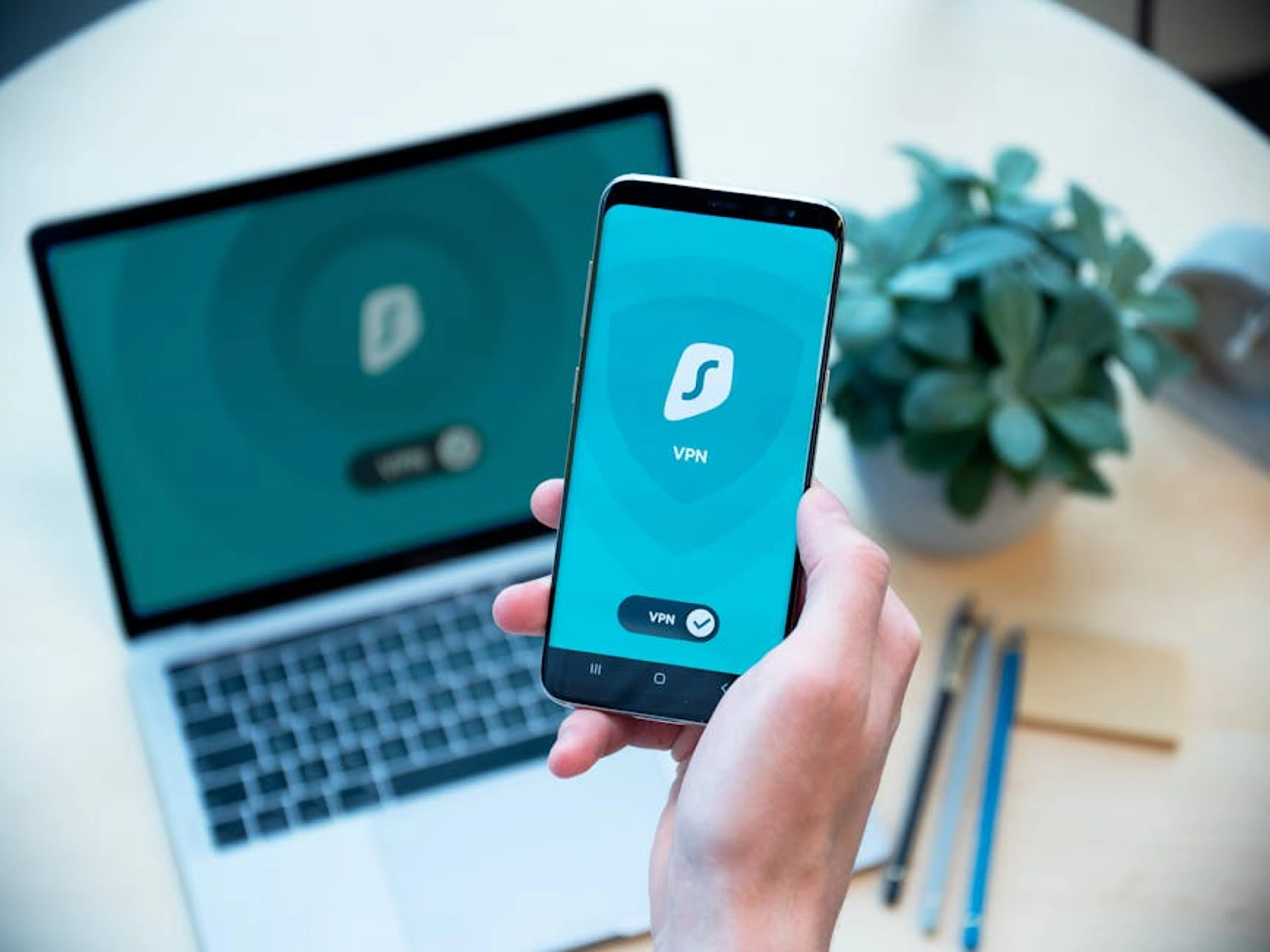 Close-up of a hand holding a smartphone with VPN app, laptop in the background, showcasing digital security. Illustration of a person's digital footprint with data flowing into a secure shield