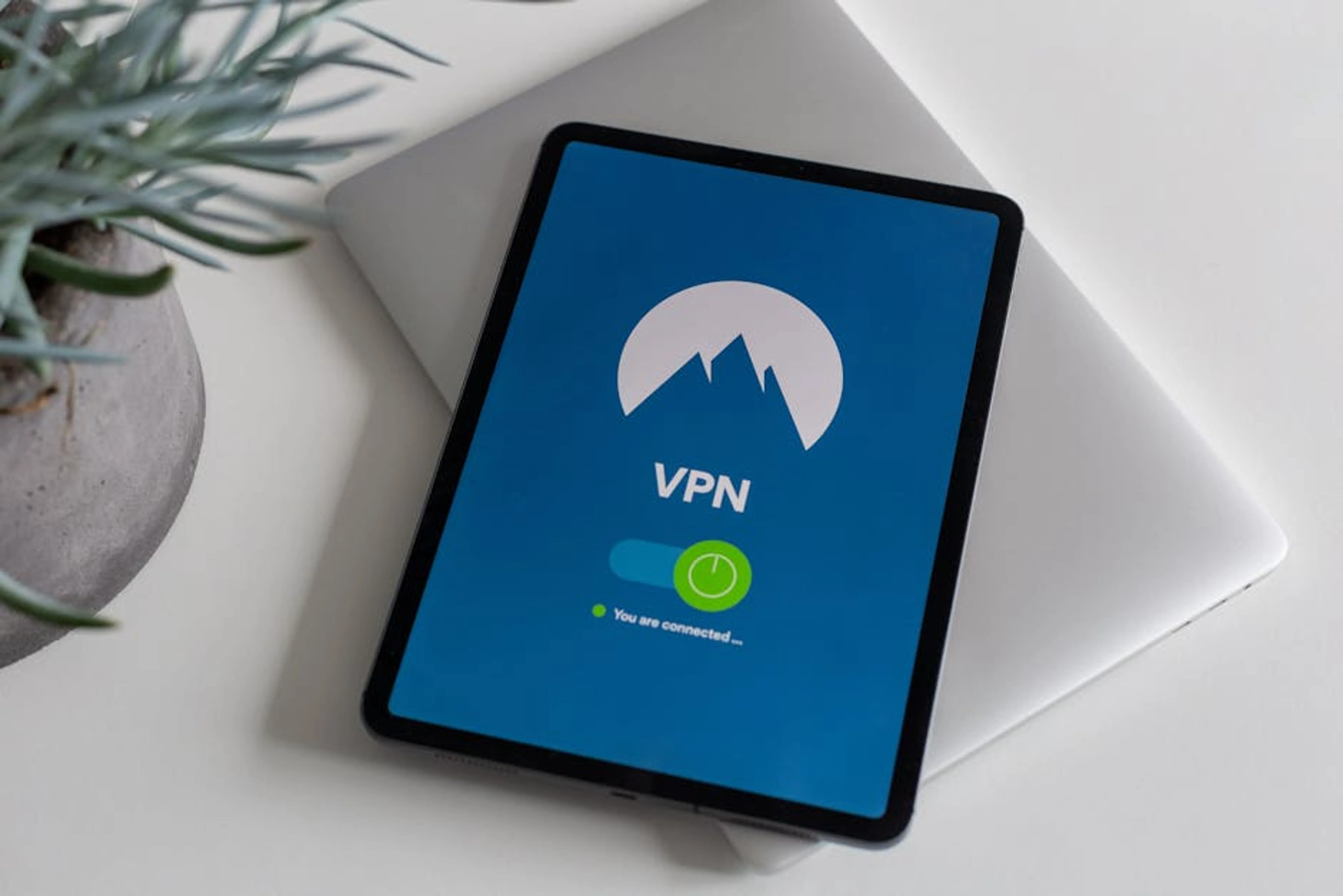 Modern tablet displaying a connected VPN app screen, symbolizing cybersecurity. Person comparing different VPN services on a laptop screen